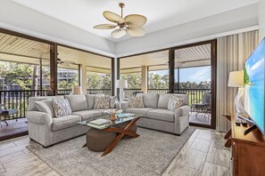 A modern living room with a sectional sofa, a glass coffee table, and a ceiling fan.
