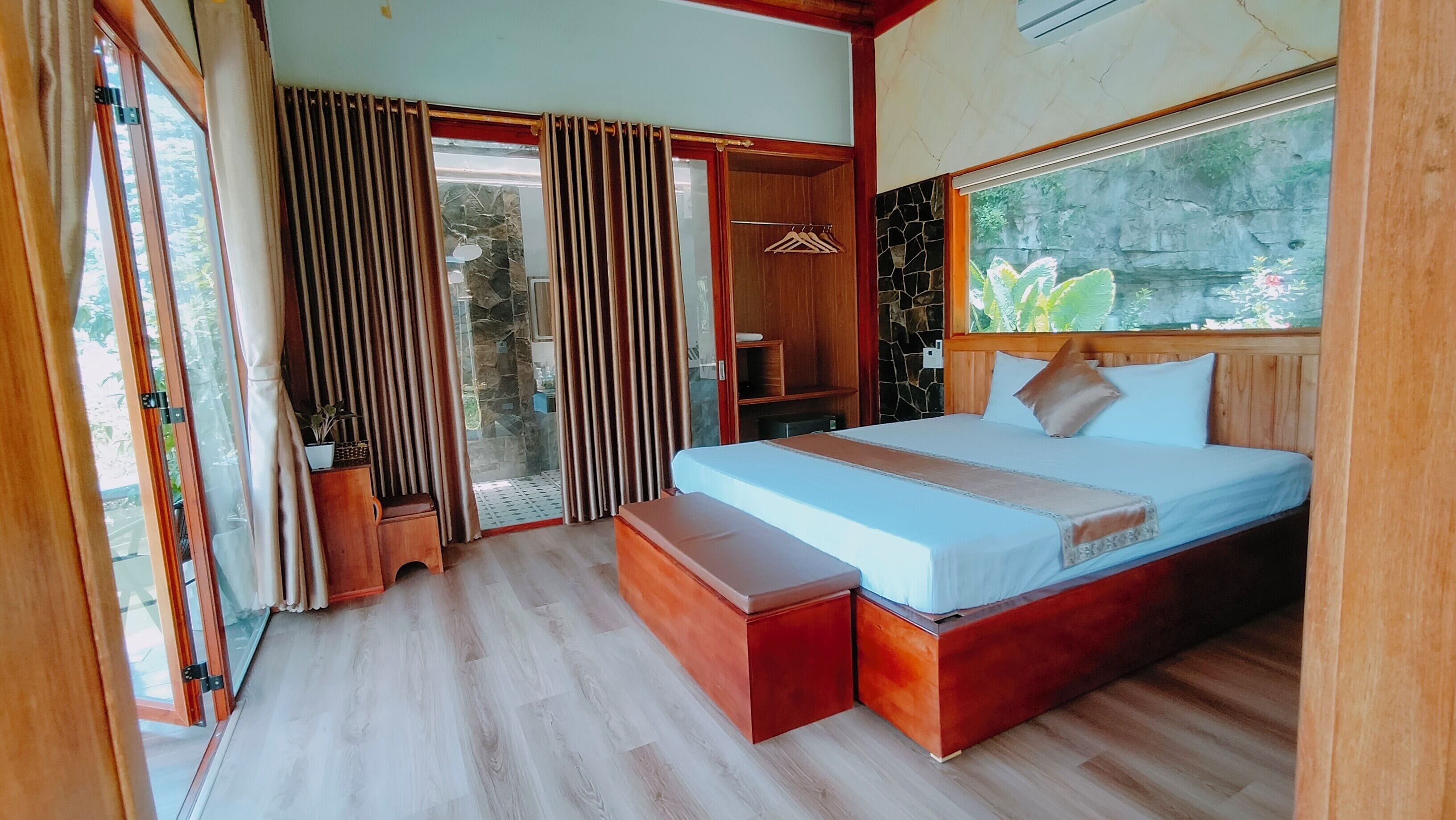 A bedroom with a large bed, wooden headboard, a bench, a wardrobe, and a sliding glass door leading to an outdoor area.
