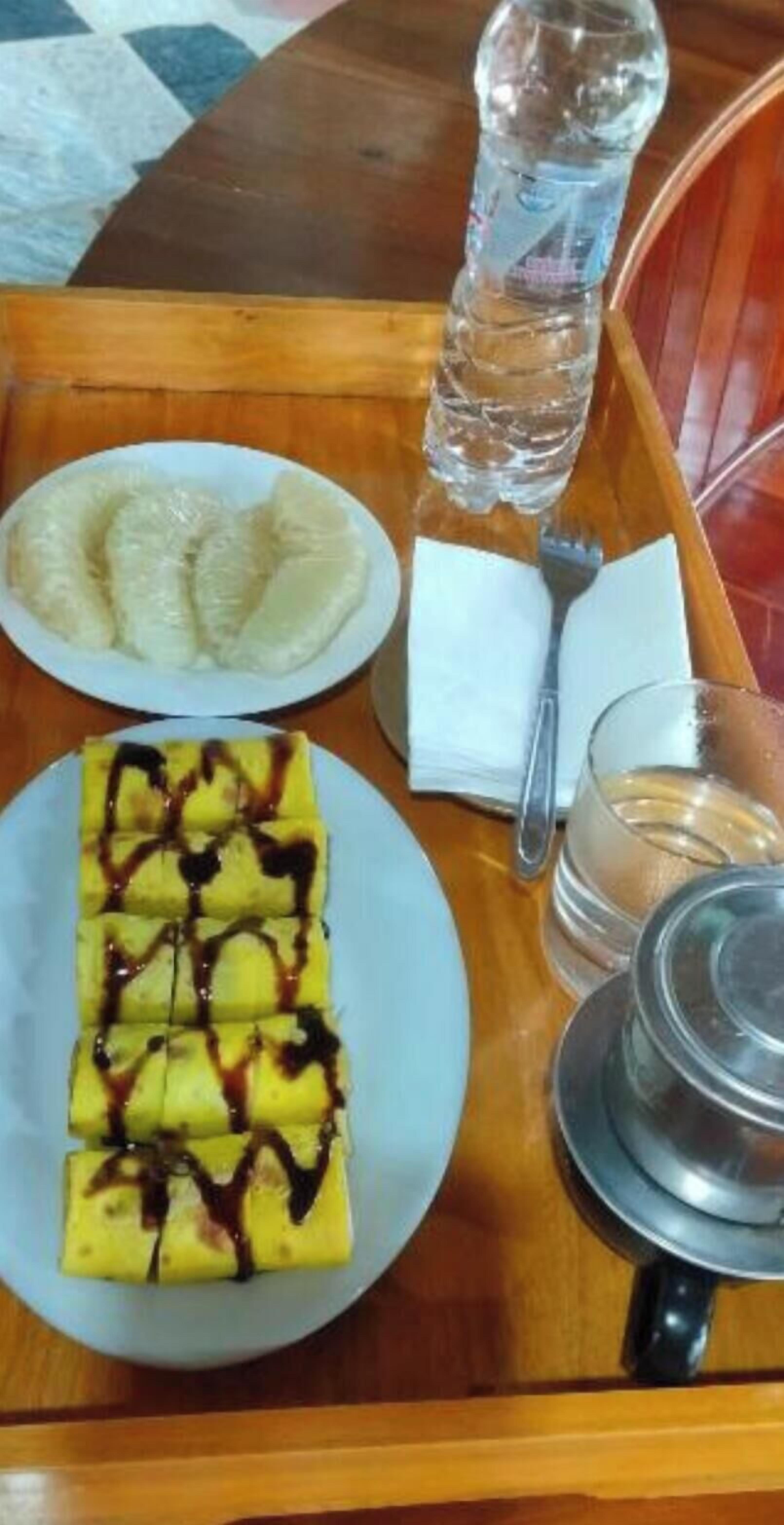 Uma bandeja com uma fatia de bananas regadas a chocolate, uma garrafa de água e um copo de água sobre uma mesa de madeira.