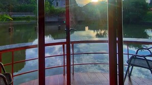 Una habitación con un gran ventanal que da a un balcón con vistas a un río y colinas al atardecer.