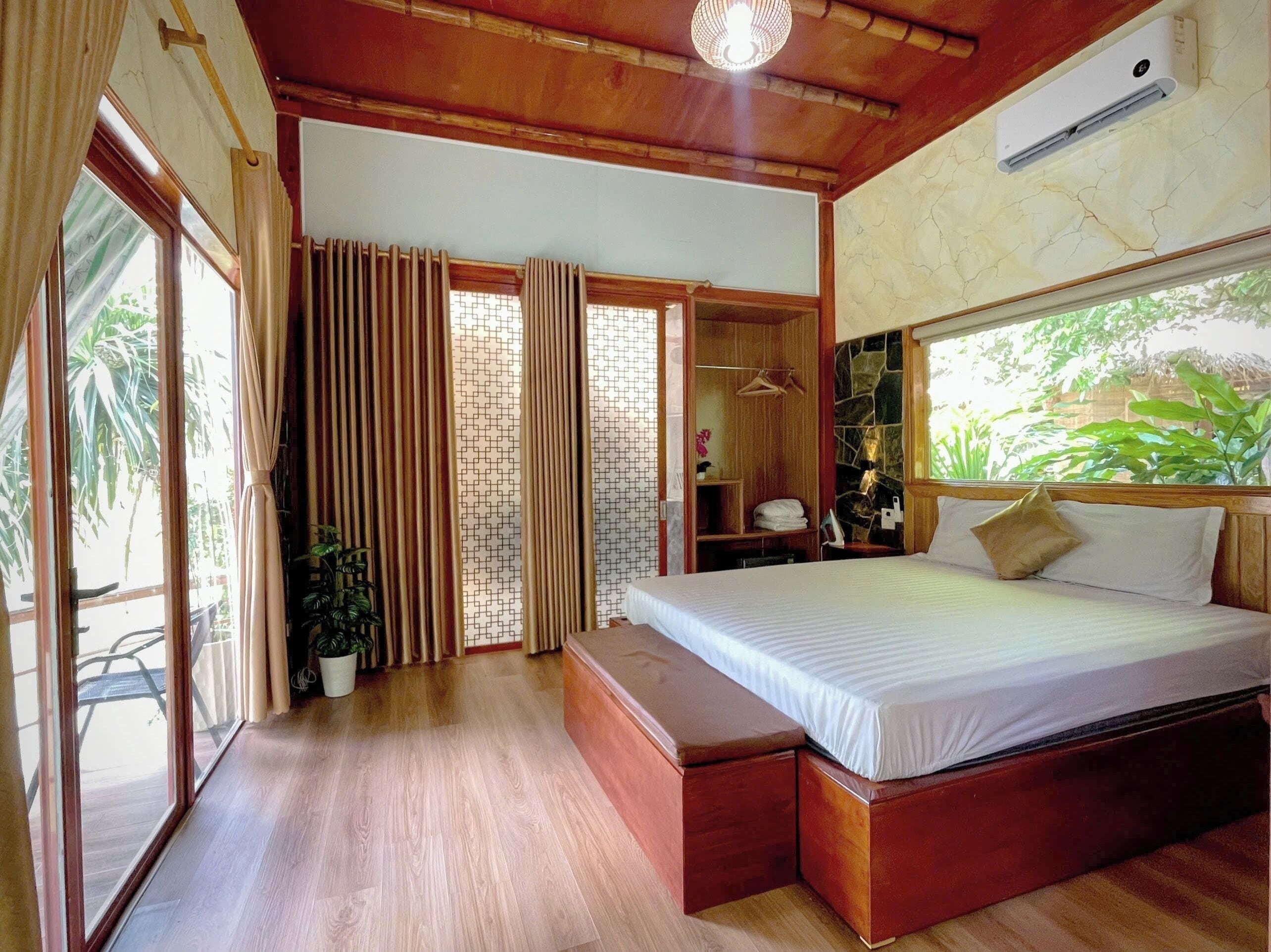 Un dormitorio con una cama grande, suelo de madera, un banco empotrado, un armario y una ventana con cortinas.