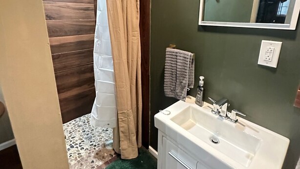 Un baño con un lavamanos blanco, paredes verdes, un espejo y una cortina de ducha.