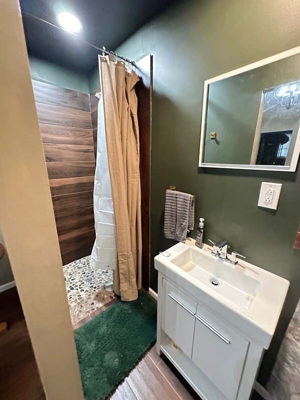 Un bagno con un lavandino bianco, pareti verdi, uno specchio e una tenda da doccia.