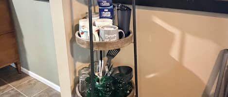 Un expositor metálico escalonado con utensilios de cocina y una cafetera.