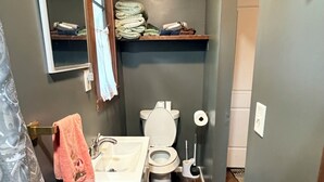 Un baño con inodoro, lavamanos y espejo sobre el lavamanos. Hay un perchero con una toalla colgada.