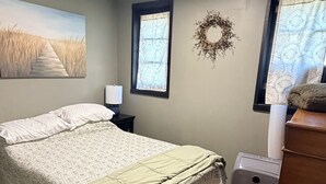 Un dormitorio con cama, mesita de noche, cómoda, radiador y ventana con cortinas.