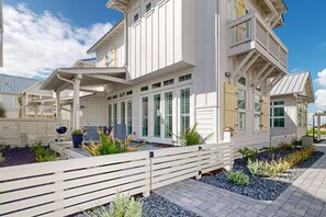 A white multi-story house with a covered patio, outdoor seating, and a landscaped garden. - Resort Style Pools, Golf Cart Boardwalk to the Beach (Port Aransas)