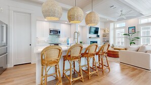 A modern kitchen with white cabinets, a central island with bar stools, and a dining area with a white sofa. - Resort Style Pools, Golf Cart Boardwalk to the Beach (Port Aransas)