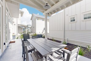 A covered patio with a wooden table and benches, surrounded by white buildings and plants. - Resort Style Pools, Golf Cart Boardwalk to the Beach (Port Aransas)