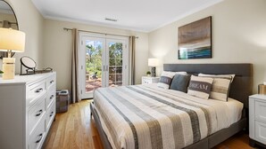 Ein Schlafzimmer mit einem großen Bett, einem Nachttisch, einer Kommode und Blick durch eine Glastür auf einen Außenbereich.