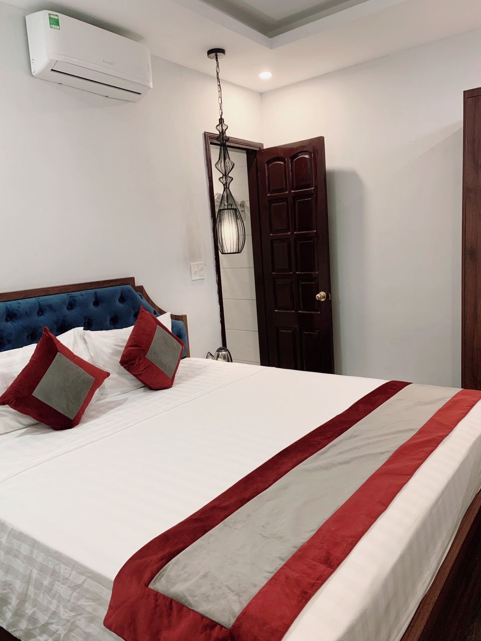 Una habitación de hotel con una cama, una puerta de madera y un equipo de aire acondicionado instalado en el techo.