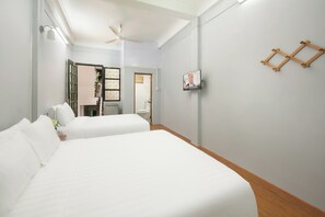 Ett hotellrum med två sängar, en takfläkt, en tv som är monterad på väggen och ett trägolv.