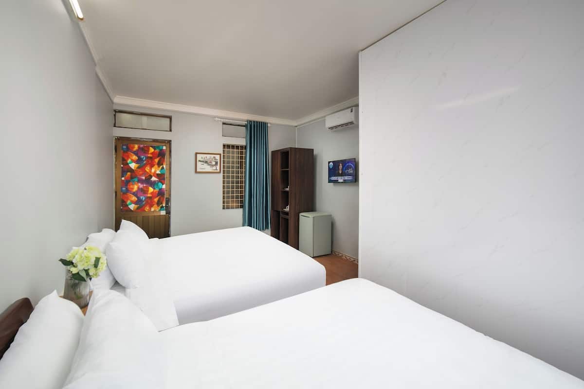Quarto de hotel com duas camas, televisão, guarda-roupa e porta decorativa.