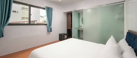 Una habitación de hotel con una cama grande, un armario, un espejo y una ventana con cortinas.