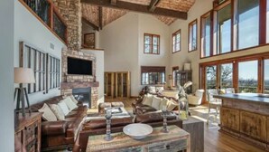 Un salón amplio con chimenea de piedra, sofás de cuero y un ventanal con vistas panorámicas.