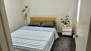 Un dormitorio con una cama, mesita de noche, lámpara y una planta en maceta.