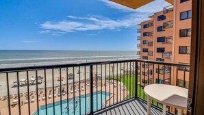 A balcony with a view of the beach and ocean, a pool, and a building with balconies. - Sunrise Delight: Oceanfront Condo w/ Pool Access (New Smyrna Beach)