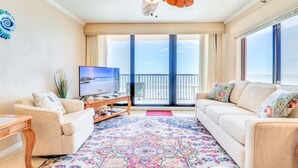 A living room with a TV, two sofas, a coffee table, and a patterned rug. - Sunrise Delight: Oceanfront Condo w/ Pool Access (New Smyrna Beach)