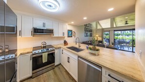 A modern kitchen with white cabinets, stainless steel appliances, and a wooden countertop. - Breathtaking Condo - Ocean View - Now With AC! (Waikoloa)