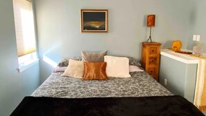 Een slaapkamer met een bed, nachtkastje, lamp en een schilderij aan de muur.