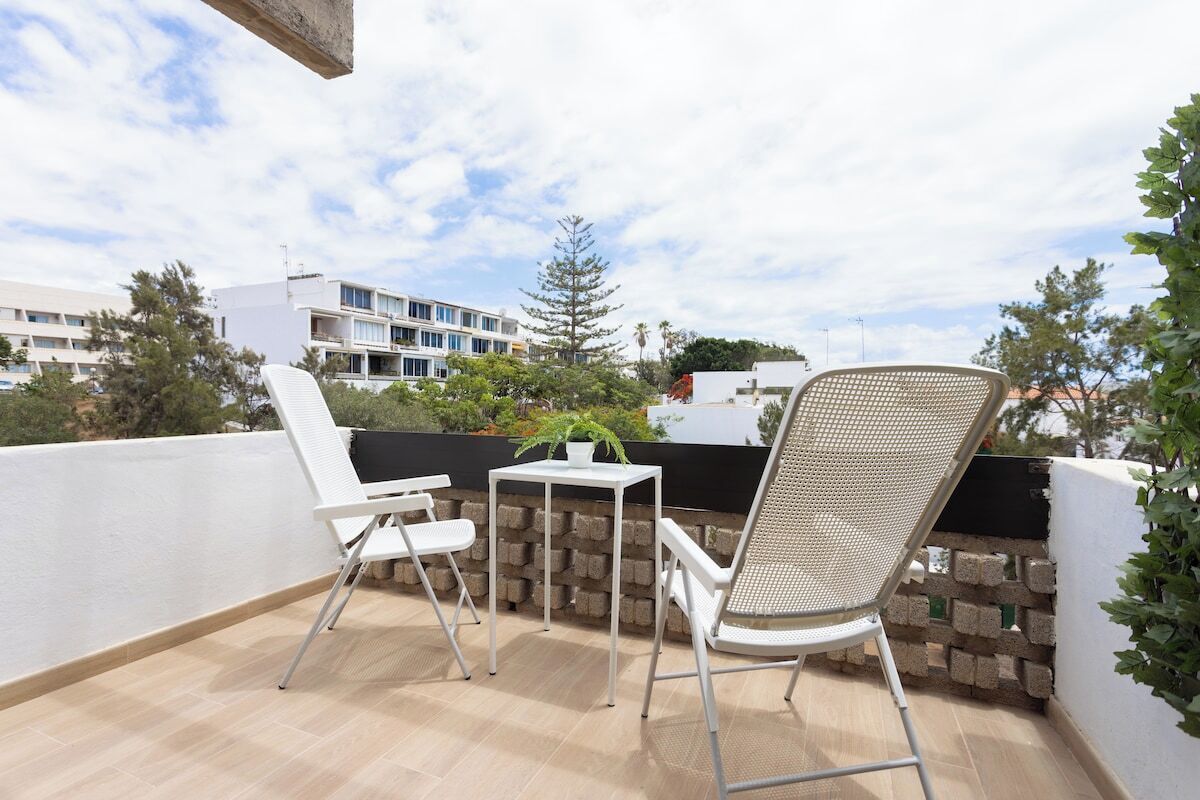 A balcony with two white chairs, a small table, and a potted plant.