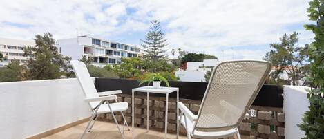A balcony with two white chairs, a small table, and a potted plant.