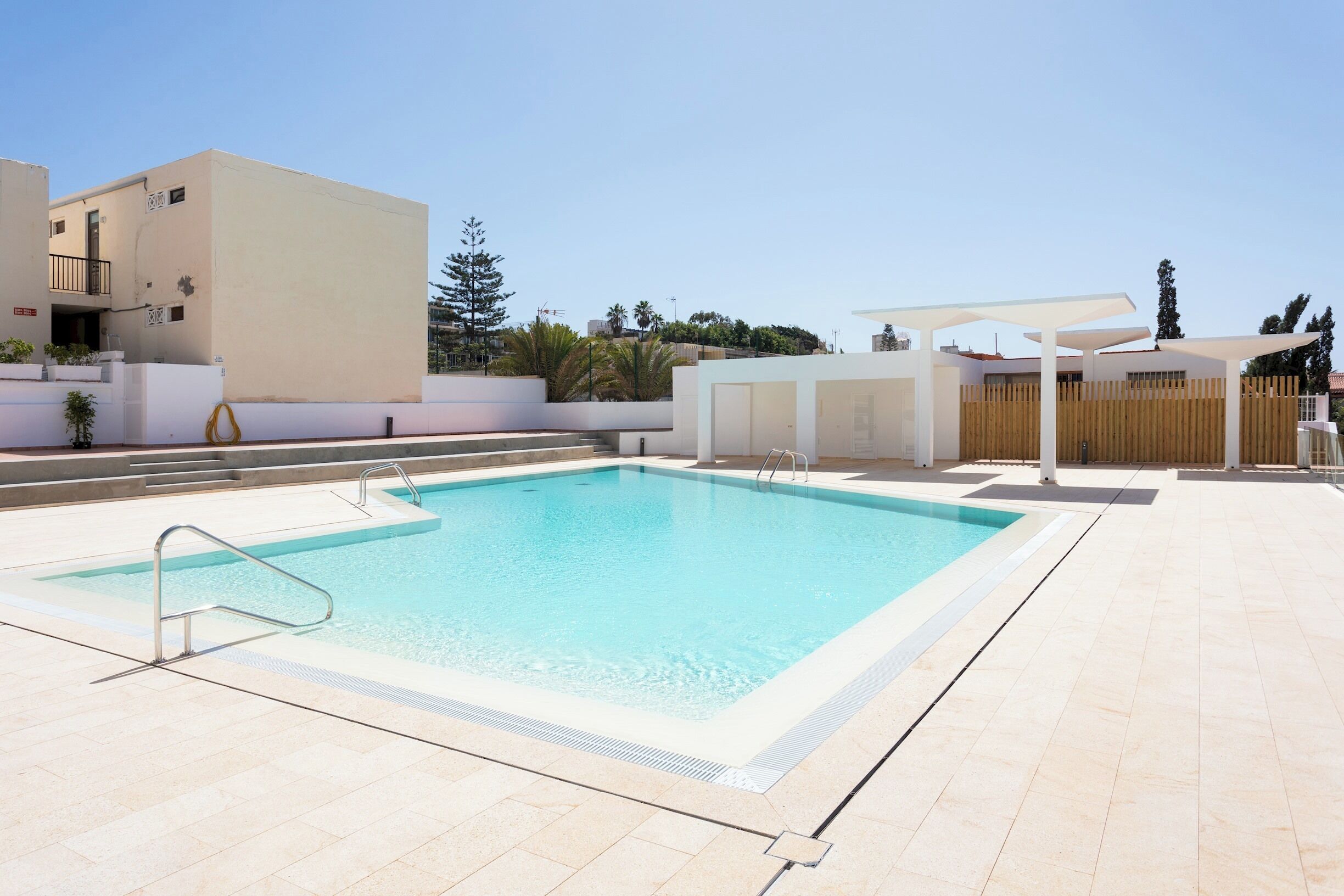 Una piscina rectangular con una escalera metálica en un lateral, rodeada por una solana con baldosas.