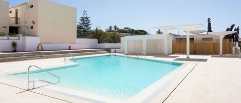 Una piscina rectangular con una escalera metálica en un lateral, rodeada por una solana con baldosas.