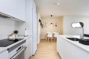 A modern kitchen with white cabinetry, a black countertop, a built-in oven, and a dining area with a table and chairs.