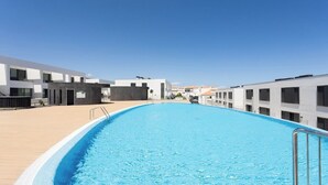 A swimming pool with a clear blue water surface, surrounded by modern buildings with balconies. - Home2Book Stylish Apartment Pool & Terrace Abades (Abades)