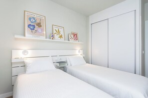 A bedroom with two beds, a white headboard, and a shelf with framed artwork. - Home2Book Stylish Apartment Pool & Terrace Abades (Abades)