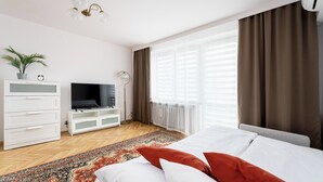 A modern hotel room with a bed, a TV, a dresser, a plant, and a large window with curtains. - Old Town Standard Studio (Kraków)