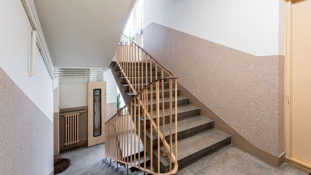 A staircase with a wooden handrail and beige walls. - Old Town Standard Studio (Kraków)