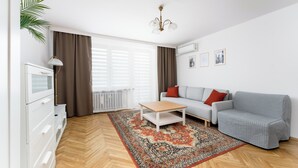 A modern living room with a sofa, a coffee table, a lamp, and a large window with curtains. - Old Town Standard Studio (Kraków)