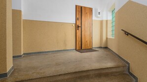 A staircase with a wooden door at the top, beige walls, and a window with a green frame. - Termy Cieplice Apartment (Jelenia Góra)