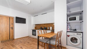A compact kitchen with white cabinets, a wooden dining table, and a built-in washing machine. - Termy Cieplice Apartment (Jelenia Góra)
