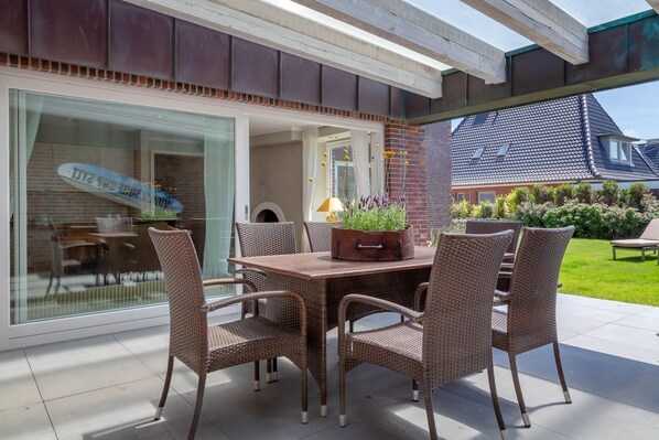 An outdoor patio with wicker furniture, a glass door leading to a room, and a brick wall.