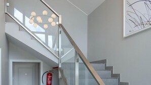 A modern staircase with glass railings and a ceiling light fixture. - Strand Cottage - Ferienwohnung "strand-cottage" in Westerland (Sylt)
