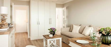 A modern living room with a wooden dining table, white sofa, and a large white wardrobe.