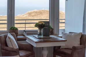 A cozy seating area with a view of the beach, a small table with a vase of flowers, and a sign with the name 'OMAPPE'. - Dünenhof zum Kronprinzen, Seafront, App. 61 - 1-room apartment with sea view and (Wenningstedt)