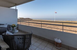 A balcony with wicker furniture, a small table with a vase, and a view of the beach and flag. - Dünenhof zum Kronprinzen, Seafront, App. 61 - 1-room apartment with sea view and (Wenningstedt)