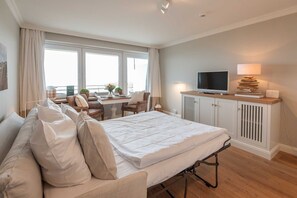 A modern hotel room with a bed, a desk, a television, and a view of the city. - Dünenhof zum Kronprinzen, Seafront, App. 61 - 1-room apartment with sea view and (Wenningstedt)