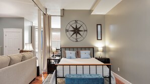 Un dormitorio con cama, mesitas de noche, un banco azul, un reloj de pared y una puerta.