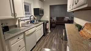 A compact kitchen with white cabinets, a microwave, and a dishwasher. There is a ceiling fan and a window with blinds. - Stay Now on the GOTL Strip! Across from Eddie's Grill, Steps from Multiple Bars (Geneva)