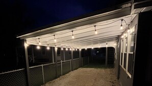 A covered outdoor area with a gravel floor, a chain-link fence, and string lights. - Stay Now on the GOTL Strip! Across from Eddie's Grill, Steps from Multiple Bars (Geneva)