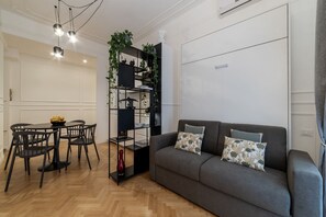 A living room with a grey sofa, black chairs, a black shelving unit with plants, and a dining table with chairs. - Toscana 2bis - FromHometoRome (Roma)