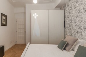 A bedroom with a bed, a wardrobe, a door, and a wall with a floral pattern.