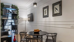 A dining area with a round table, four chairs, a black bookshelf with plants, and two framed pictures on the wall. - Toscana 2bis - FromHometoRome (Roma)