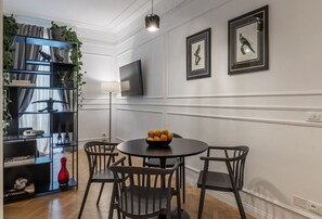 A dining area with a round table, four chairs, a black bookshelf with plants, and two framed pictures on the wall. - Toscana 2bis - FromHometoRome (Roma)