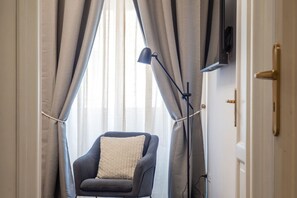 A room with a chair, a floor lamp, and a TV mounted on the wall. - Toscana 5 - FromHometoRome (Roma)